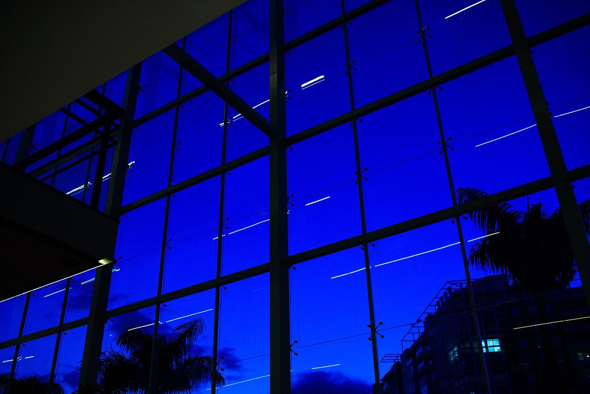 vista interna, através de janela de vidro, com céu azul ao fundo.